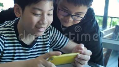 慢动作4K快乐的亚洲男孩一起在智能手机上在线玩手机游戏。 有福的男孩和朋友商量策略